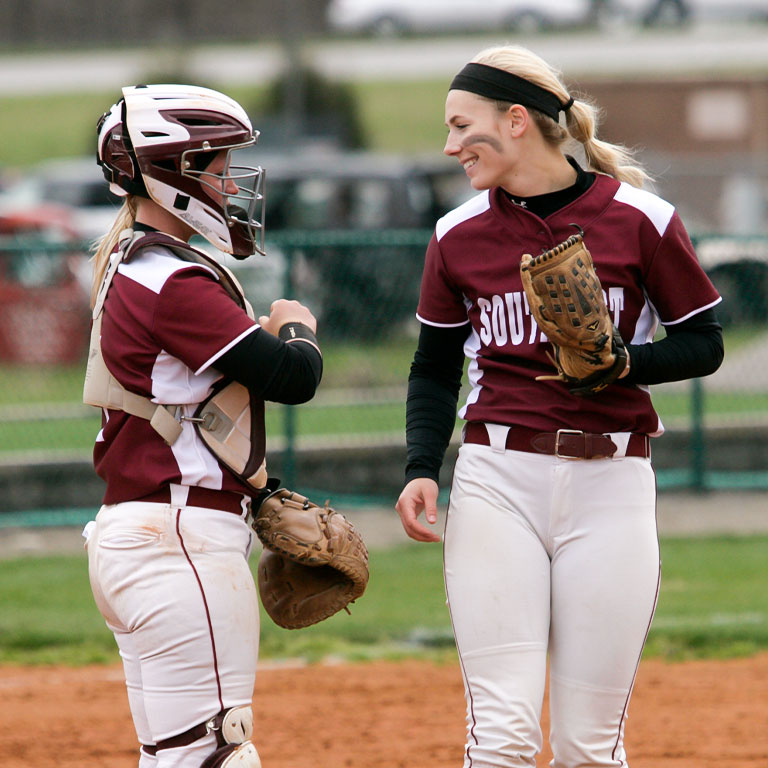 Two IU Southeast softball players smiling and talking to each other